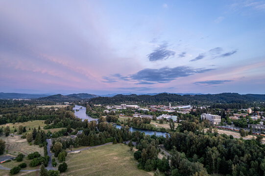Aerial view of the serene Willamette River meandering through lush greenery, past the University of Oregon campus under a pastel sky, Eugene, Oregon, United States.