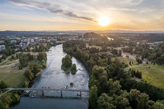 Aerial view of the Willamette River gently flowing under a bridge, reflecting the golden sunset near Alton Baker Park, Eugene, Oregon, United States.