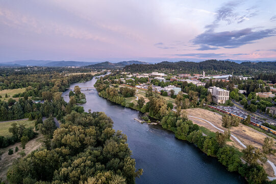 Aerial view of the Willamette River winding through lush greenery, with glimpses of the University of Oregon campus under a serene sky, Eugene, Oregon, United States.