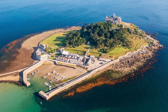 Aerial view of St Michael's Mount rising majestically from the turquoise sea, crowned with its ancient castle, a beacon of history against the horizon, Marazion, England, United Kingdom.