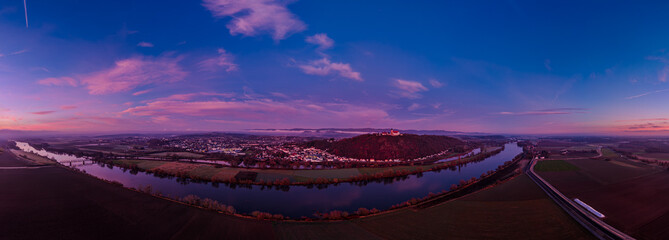 Sonnenuntergang über der Stadt am Fluss mit Bergen im Hintergrund