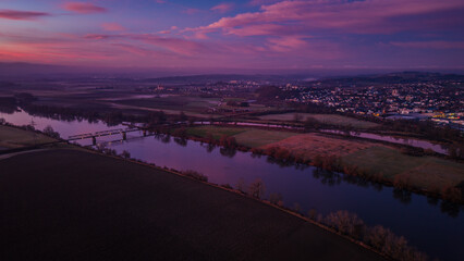 Blick auf die Landschaft bei Sonnenuntergang &uuml;ber einem Fluss und der Stadt im Hintergrund