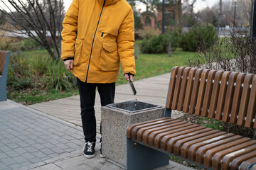 A person wearing a yellow coat discards an object into a trash can in a park