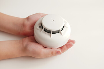Child’s hands holding a white smoke detector, symbolizing home fire safety, prevention and...