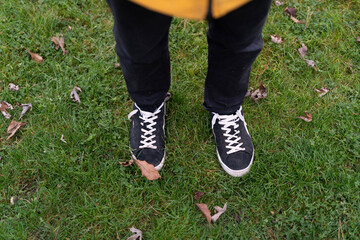 Person stands on green grass with fallen leaves, wearing black shoes and black pants