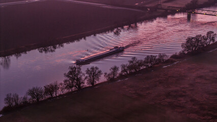 Ein Schiff f&auml;hrt auf dem Fluss bei Sonnenuntergang in einer l&auml;ndlichen Umgebung mit B&auml;umen am Ufer