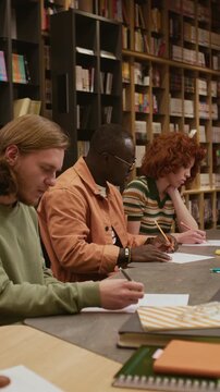 Vertical side view shot of focused Black man looking up answers at groupmates paper while writing examination test in language training course for adults in library