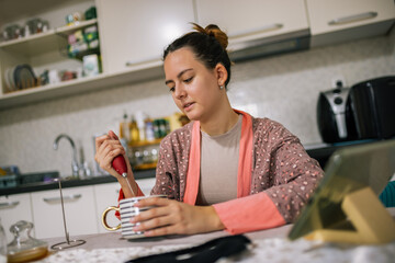 Fototapeta premium Young woman at home stirs her instant coffee with a hand whisk, preparing her morning drink.
