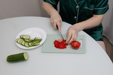A woman chopping vegetables for a salad on a cutting board, close-up of her hands. Healthy eating concept