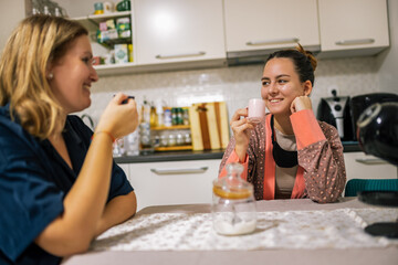 A mother and her daughter sit at home, enjoying their morning coffee together in a relaxed atmosphere.