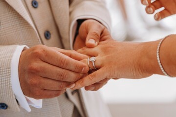 Groom placing a beautiful diamond wedding ring onto the finger of the bride during the sacred and...