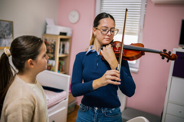 The instructor shows the girl how to hold the violin and move the bow correctly during an at-home...