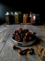 A small bowl filled with dried cloves sits on a dark wooden surface.