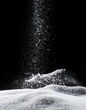 White Granules Falling Onto a Pile of White Granules Against a Black Background