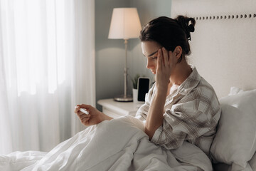 Female in pajamas, sitting on bed, holding pregnancy test  with a worried expression, surrounded by soft light reflecting a moment of health concern