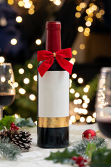 A bottle of red wine and red ribbon bow with Christmas decoration, light illumination, festive ambiance, glass of wine, illuminated light bokeh in background.