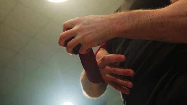 Boxer puts bandages on hands before fight in special hall. Athlete prepares to start training and strengthens muscles with elastic fabric