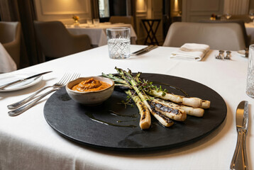 Cal&ccedil;ots gourmet emplatados con salsa romesco en restaurante de alta cocina, presentados sobre plato de pizarra negra sobre mantel blanco en un entorno elegante y moderno.
