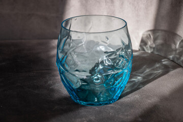 A textured blue glass tumbler catches soft light on a dark fabric surface.