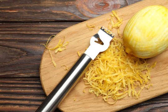 Lemon zest, fresh fruit and zester tool on wooden board, top view