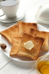 Fresh toasted bread slices served with butter, honey and tea on white wooden table