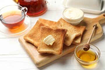 Fresh toasted bread slices served with butter, honey and tea on white wooden table