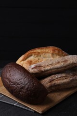 Different types of bread loaves on black table, closeup