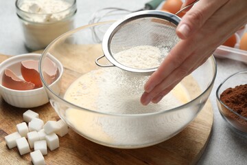 Making dough. Woman sieving flour into bowl and different ingredients at grey table, closeup