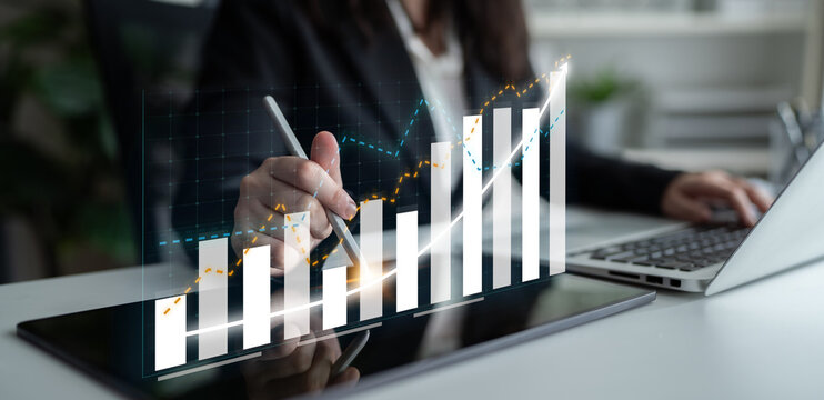 A business professional engages in financial analysis using digital graphs and charts, highlighting growth trends in a modern office setting. Impute - Powered by Adobe