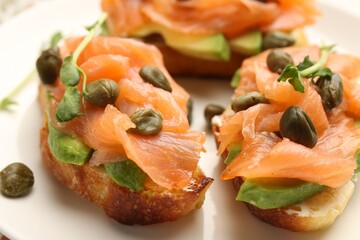Tasty bruschettas with salmon, avocado, capers and microgreens on table, closeup