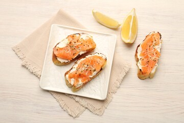 Tasty bruschettas with salmon, cream cheese, microgreens and lemon slices on light wooden table, flat lay