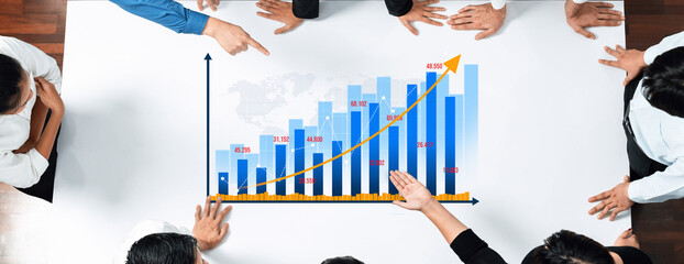 A diverse group of professionals engaged in a collaborative meeting, analyzing a vibrant growth chart in a modern office setting, illustrating progress and teamwork. Amity
