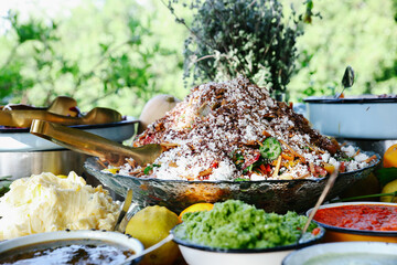 Large Catering Bowl of Layered Grain and Vegetable Salad Topped with Feta or Cheese and Nuts, Part of a Rustic Outdoor Buffet Spread