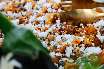 Close-up of Rustic Roasted Butternut Squash and Vegetable Salad Topped with Crumbled Feta Cheese and Chopped Hazelnuts, Served with Golden Tongs