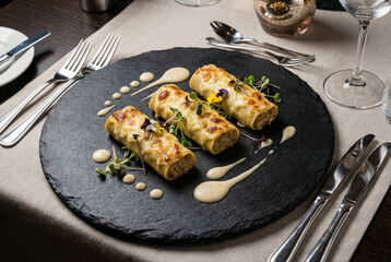 Canelones gratinados con bechamel y brotes frescos sobre pizarra en restaurante gourmet.