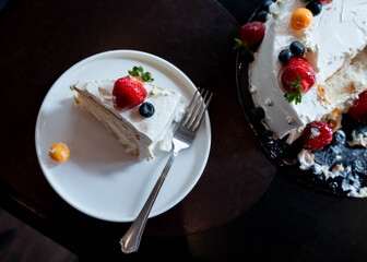 delicious piece of creamy cake with strawberries and blueberries lying near the whole cake