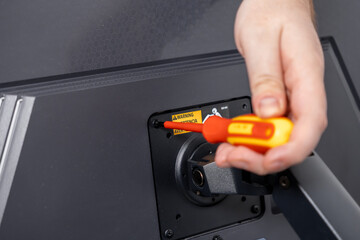 Close-up of a hand using a red and yellow screwdriver to remove a screw from a monitor mount,...