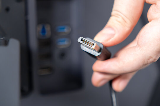 Hand holding DisplayPort cable connector, preparing connection to computer, symbolizing digital data transmission, display setup, and essential technology integration