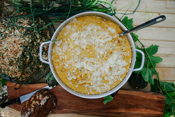 Overhead View of Creamy Yellow Polenta or Hominy Topped with Large Cheese Shavings in a Metal Pan at a Rustic Outdoor Buffet