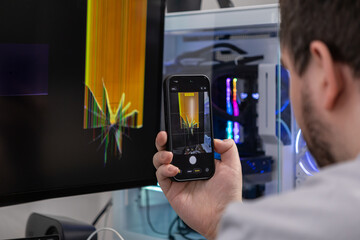 Man capturing a broken computer monitor's screen displaying visual artifacts using a smartphone, for technical support and repair documentation