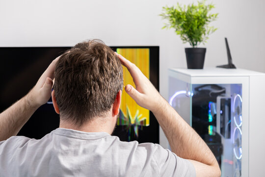 Frustrated man with hands on head stares at a computer monitor showing a glitched display, symbolizing technical issues, system errors, and digital stress