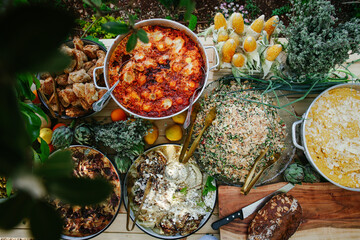 Full Overhead View of a Rustic Outdoor Catering Buffet Spread Featuring Savory Casseroles, Quinoa Salad, Breads, Corn, and Fresh Herbs for a Special Event