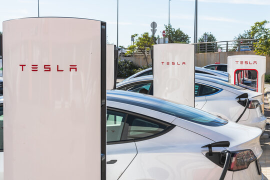Several Tesla electric vehicles are parked side by side while charging at a full Supercharger station.
