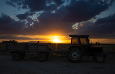 A tractor in a farmland at sunset.