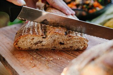 Close-up of a Serrated Knife Slicing a Rustic Loaf of Sourdough Bread on a Wooden Cutting Board, Showing the Freshly Baked Interior