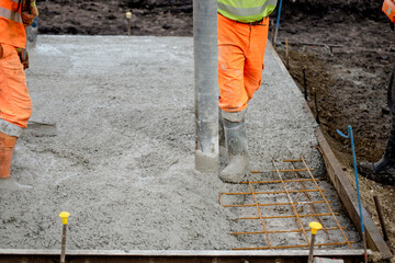 Construction worker operating a concrete pump at a job site in the daytime, focusing on the pouring process and surrounding activity