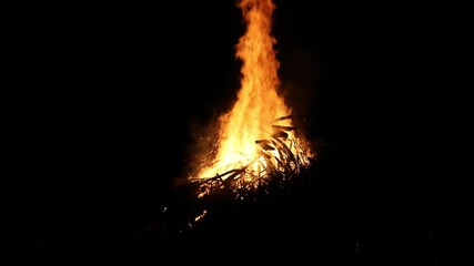 bonfire flames rising into dark night sky (bon fire flame orange yellow red glow glowing ember) sticks wood stick brush wooden fuel summer ceremony celebration enormous huge rise heat campfire camping