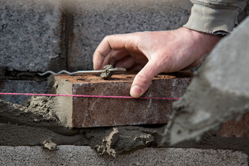 Bricklayer builder working laying red bricks on construction site