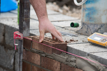 Industrial bricklayer laying bricks and concrete blocks on cement mix mortar on construction site