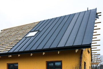 Naklejka premium Modern house roof renovation with black metal panels and skylight during construction process